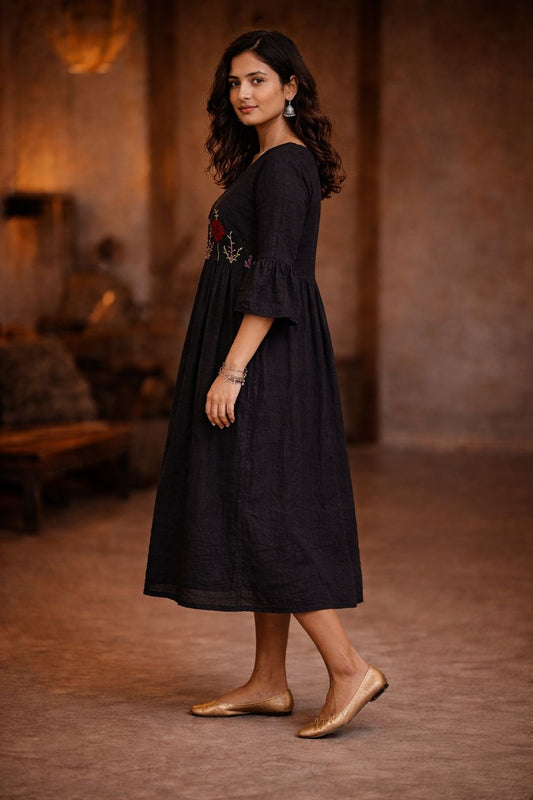 Woman wearing a black dress with floral embroidery in a warm-toned room.