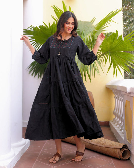 Woman wearing a black dress standing in a room with green plants and a white column.