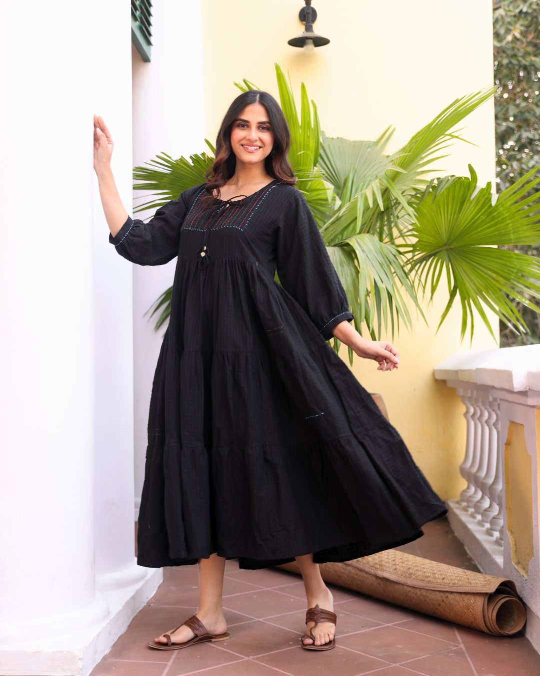 Woman in a black dress standing in a room with plants and a white wall.