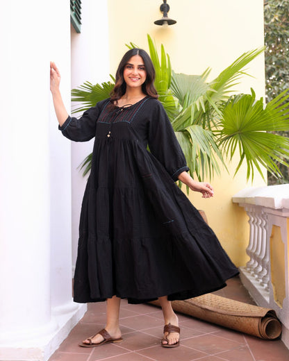 Woman in a black dress standing in a room with plants and a white wall.