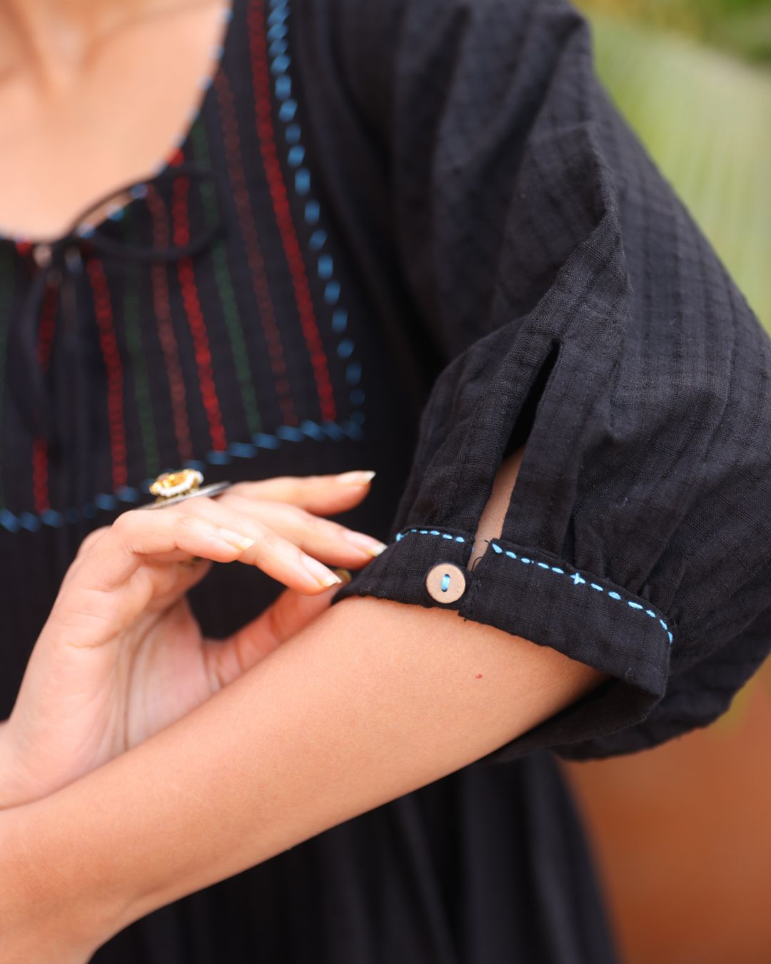 Close-up of a person wearing a black shirt with rolled-up sleeves and a colorful striped garment underneath.