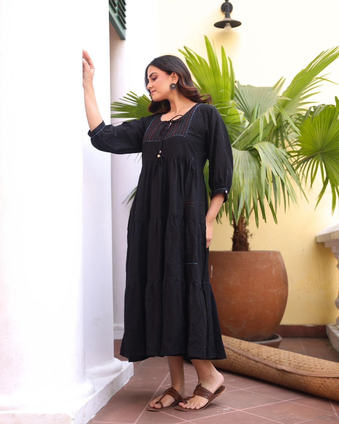 Woman in a black dress standing in a room with plants and a white wall.