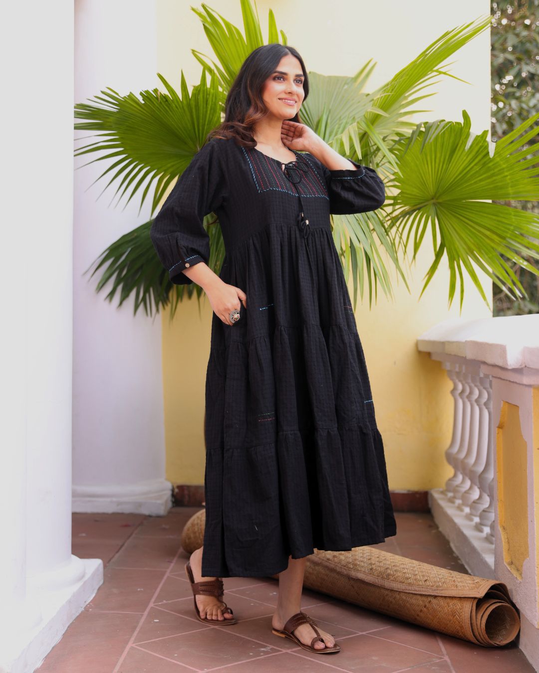 Woman in a black dress standing in front of a white wall with green plants