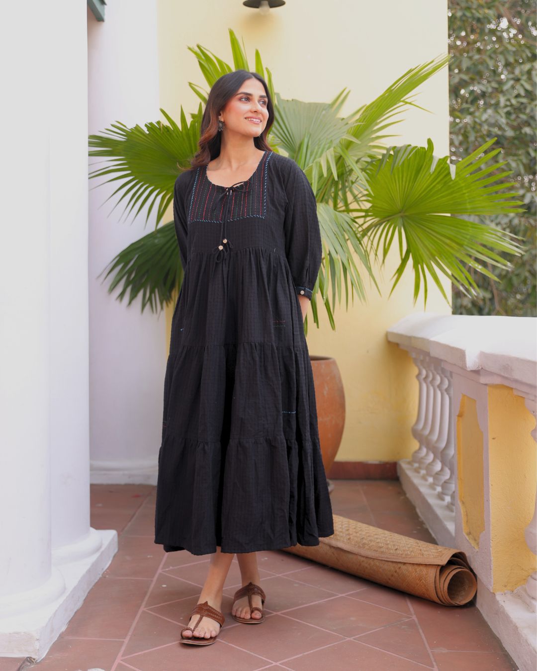 Woman in a black dress standing in front of a yellow wall with green plants