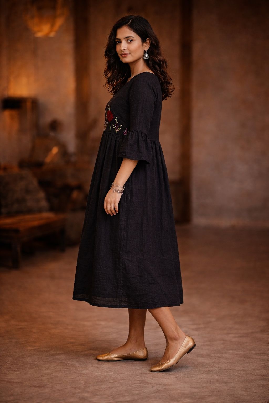 Woman wearing a black dress with floral embroidery in a warm-toned room.
