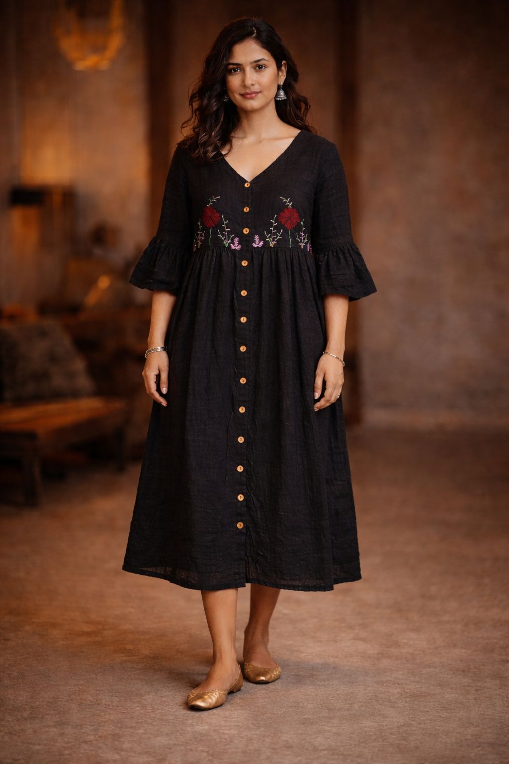 Woman wearing a black dress with floral embroidery in a warm-toned room.