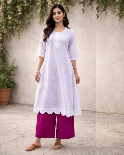 Woman wearing a white kurta with pink pants against a neutral background