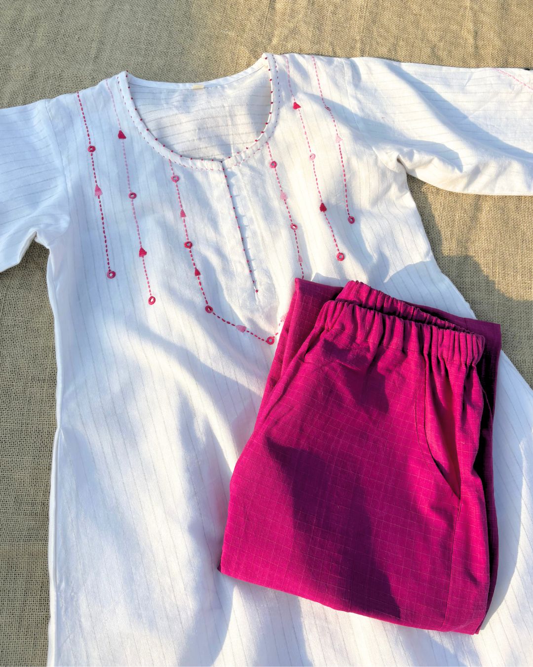 White top with red embellishments and pink pants on a textured surface