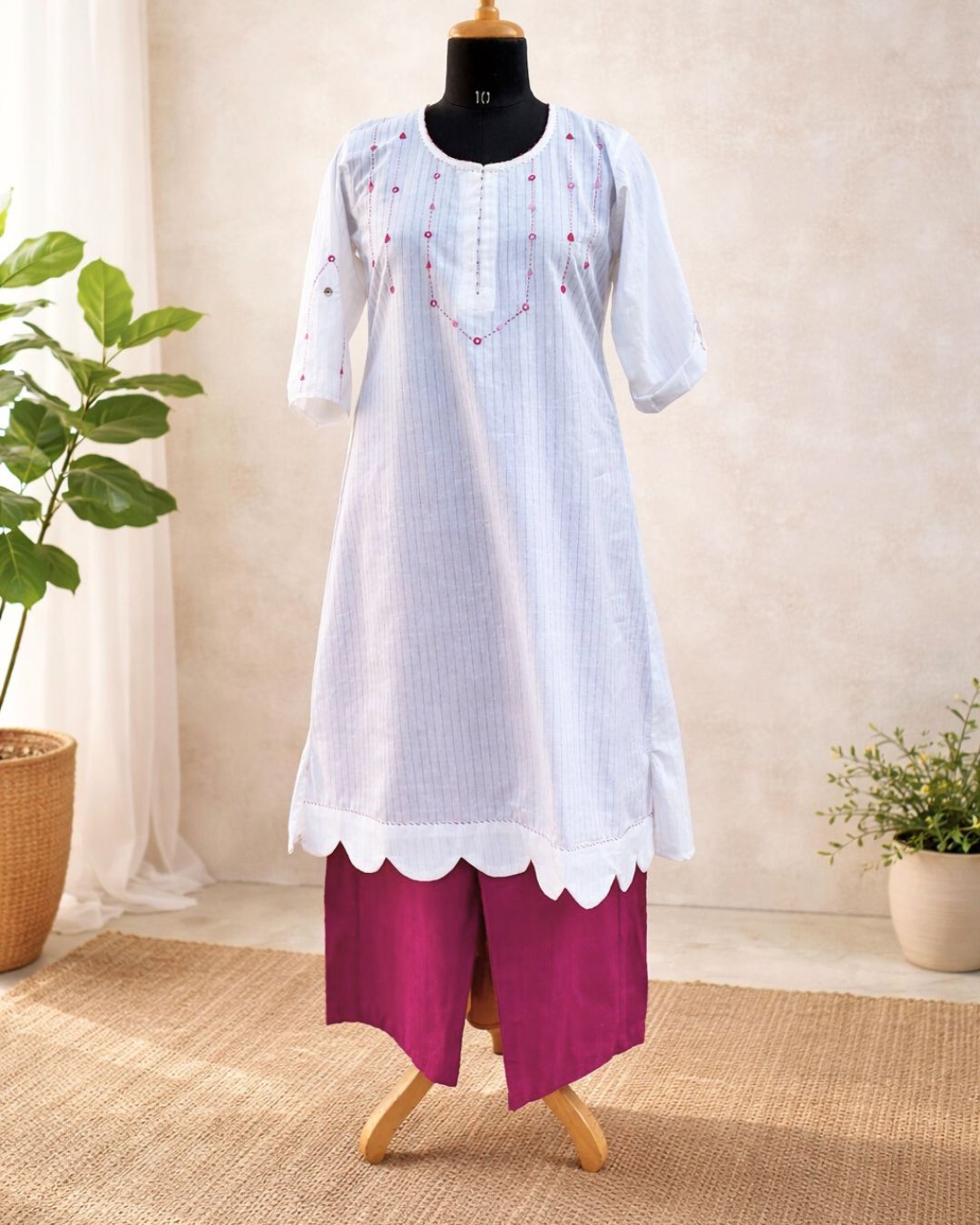 White kurta with  scalloped hem and pink pants on a mannequin against a neutral background.